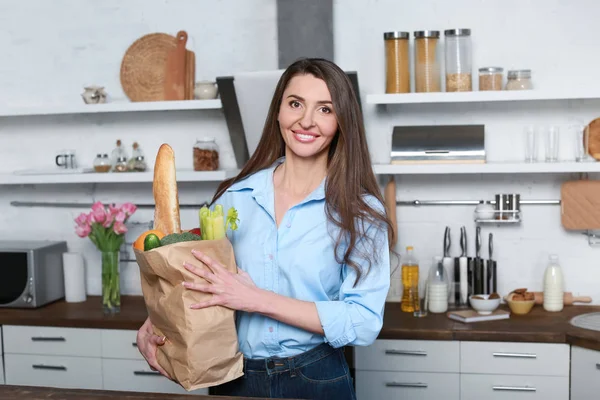 Hermosa mujer con bolsa llena de productos en la cocina en casa —  Fotos de Stock