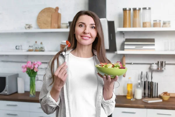 Mulher bonita comendo salada saudável na cozinha em casa — Fotografia de Stock
