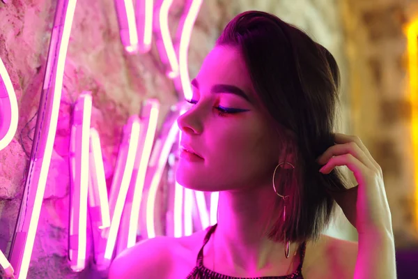 Toned portrait of beautiful young woman near neon lighting on wall — Stock Photo, Image