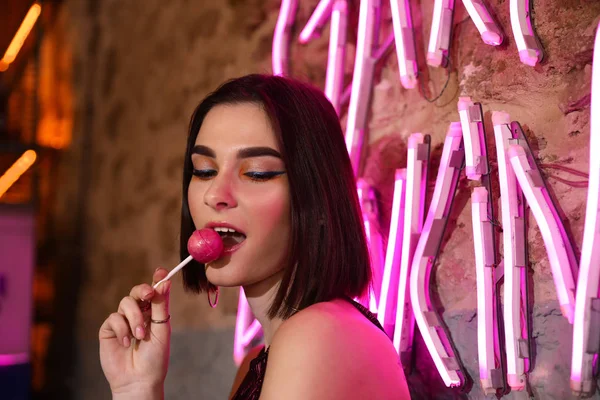 Portrait of beautiful young woman near neon lighting on wall — Stock Photo, Image