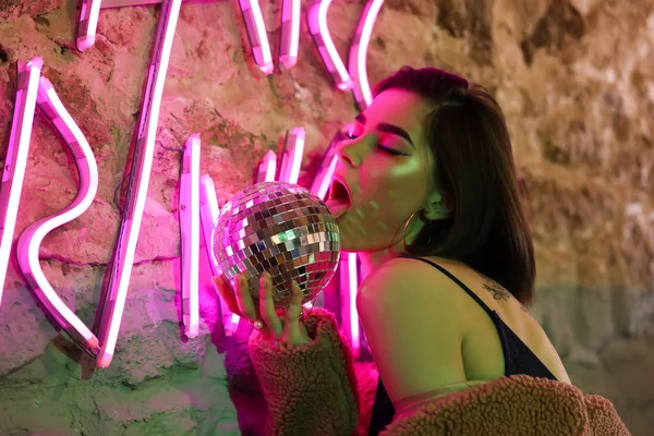 Toned portrait of beautiful young woman with disco ball near neon lighting on wall — Stock Photo, Image
