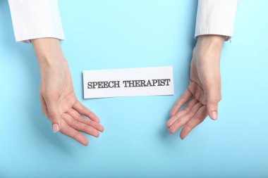 Doctor's hands and paper with text SPEECH THERAPIST on color background clipart