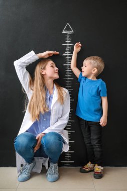 Küçük çocuk karanlık duvarının yakınında yükseklik ölçme ile kadın doktor