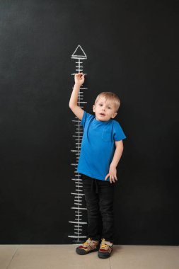 Küçük çocuk karanlık duvarının yakınında yükseklik ölçme