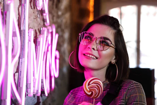 Toned portrait of beautiful young woman near neon lighting on wall — Stock Photo, Image