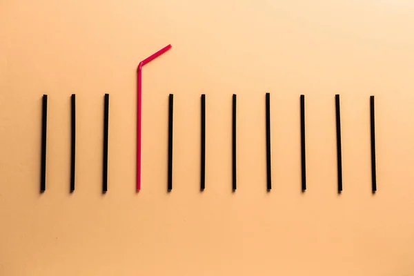Rode cocktail stro onder zwarte degenen op kleur achtergrond. Concept van uniciteit — Stockfoto