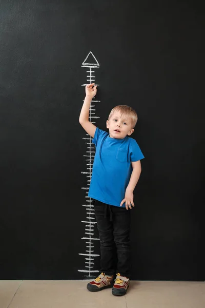 Little boy measuring height near dark wall — Stock Photo, Image