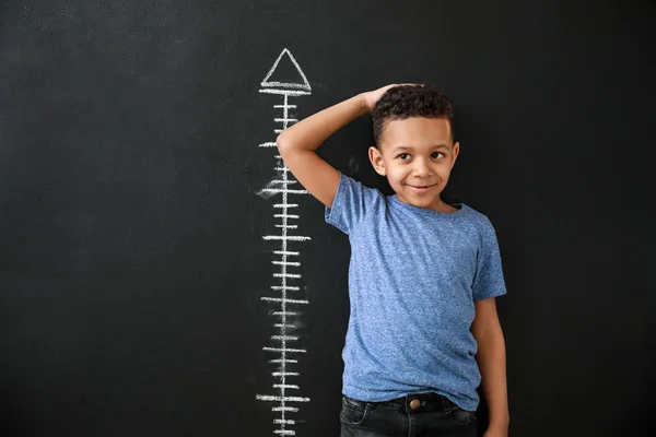 African-American boy measuring height near dark wall — Stock Photo, Image