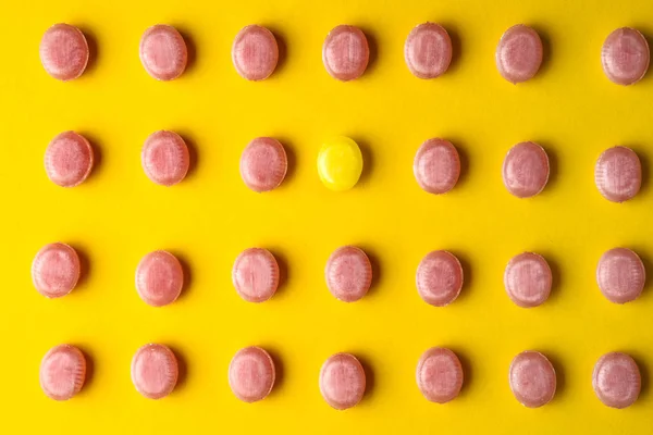 One yellow candy among pink ones on color background. Concept of uniqueness