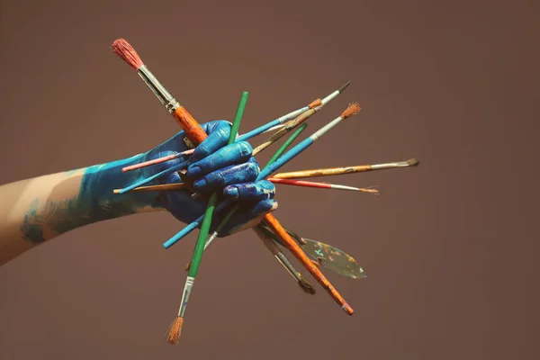 Mano femminile dipinta con pennelli su sfondo a colori — Foto Stock