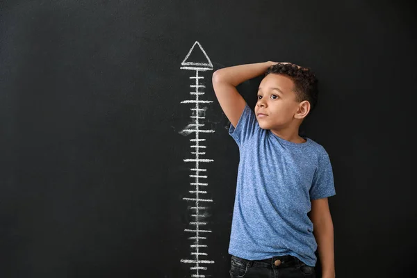 Niño afroamericano midiendo altura cerca de la pared oscura —  Fotos de Stock