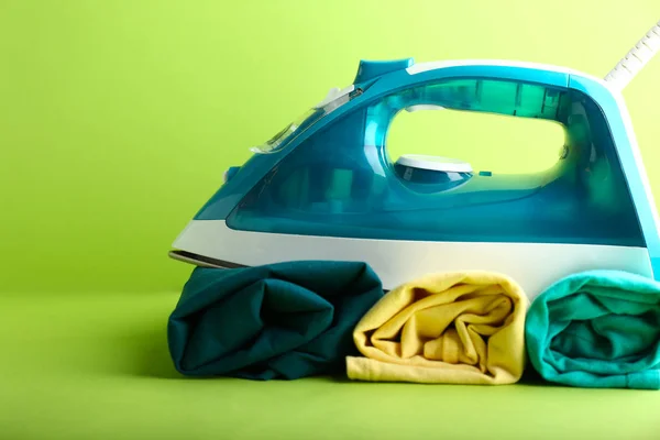 Iron with clean clothes on color background — Stock Photo, Image