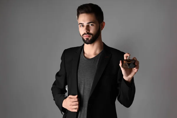 Schöner Mann mit einer Flasche Parfüm auf grauem Hintergrund — Stockfoto
