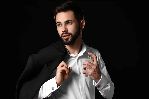 Homem bonito com garrafa de perfume no fundo escuro — Fotografia de Stock