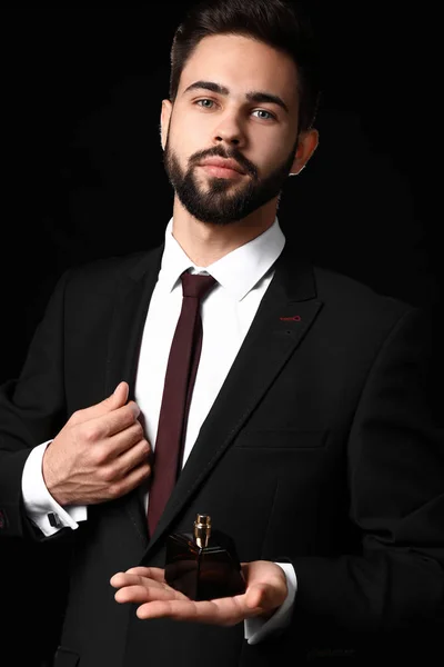 Handsome man with bottle of perfume on dark background — Stock Photo, Image