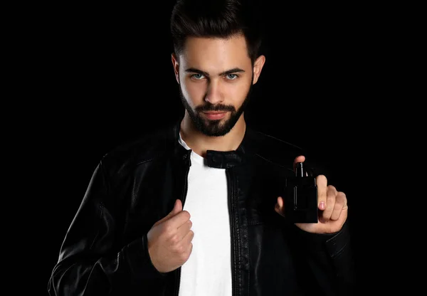 Homem bonito com garrafa de perfume no fundo escuro — Fotografia de Stock