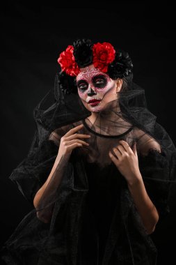 Yüzünde koyu arka plan karşı ölülerin Meksika'nın günü için boyalı kafatası ile genç kadın