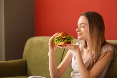 Güzel genç kadın kanepede oturan lezzetli hamburger ile