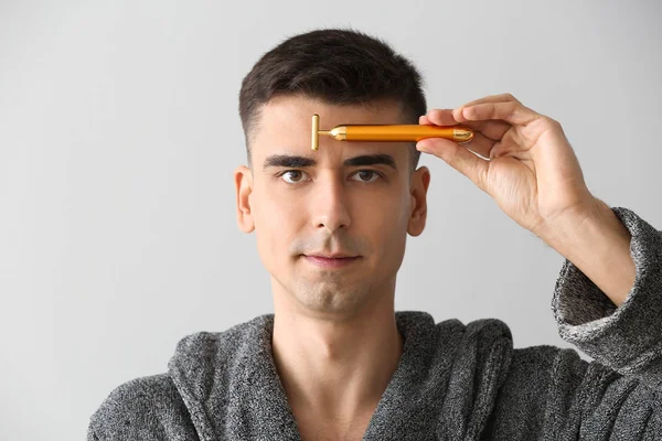 Man met gezichtsmassage tool op lichte achtergrond — Stockfoto
