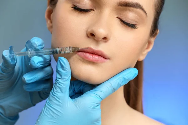 Junge Frau erhält Injektion ins Gesicht vor farbigem Hintergrund — Stockfoto