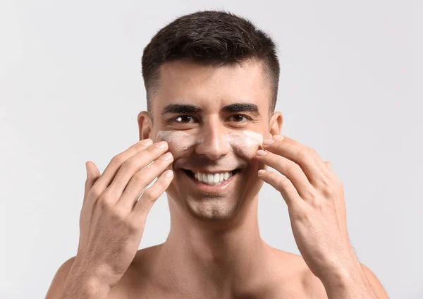Mann mit aufgesetztem Gesichtsserum gibt sich Gesichtsmassage auf hellem Hintergrund — Stockfoto