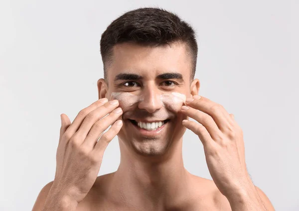 Uomo con siero viso applicato dandosi massaggio viso su sfondo chiaro — Foto Stock