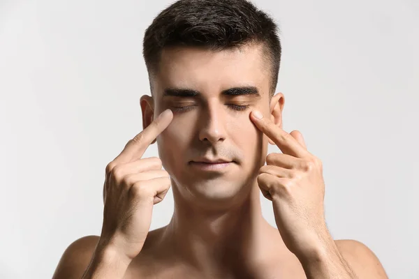 Hombre dándose masaje facial sobre fondo claro — Foto de Stock