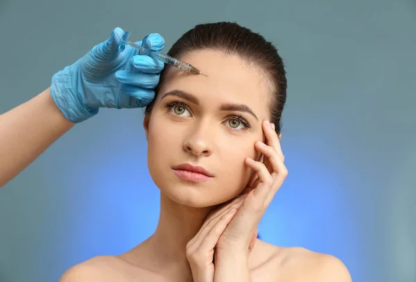 Young woman receiving injection in face on color background — Stock Photo, Image