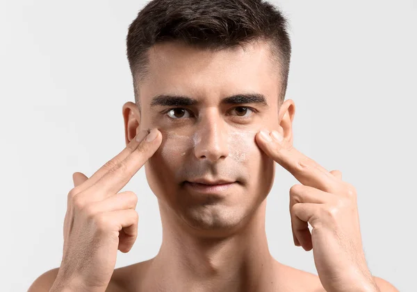 Man with applied face serum giving himself face massage on light background — Stock Photo, Image