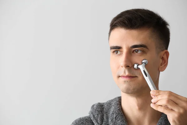 Man met gezichtsmassage tool op lichte achtergrond — Stockfoto