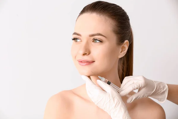 Mladá žena podáním injekce do obličeje na světlé pozadí — Stock fotografie