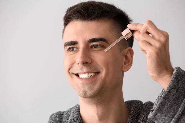 Handsome man applying face serum on light background — Stock Photo, Image