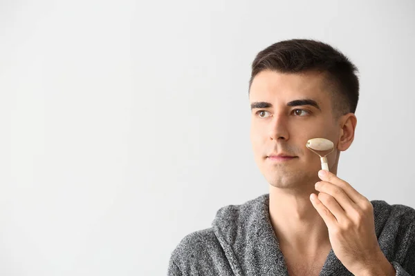 Uomo con strumento di massaggio facciale su sfondo chiaro — Foto Stock