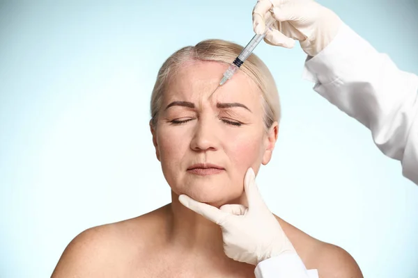 Mature woman receiving injection in face on color background — Stock Photo, Image