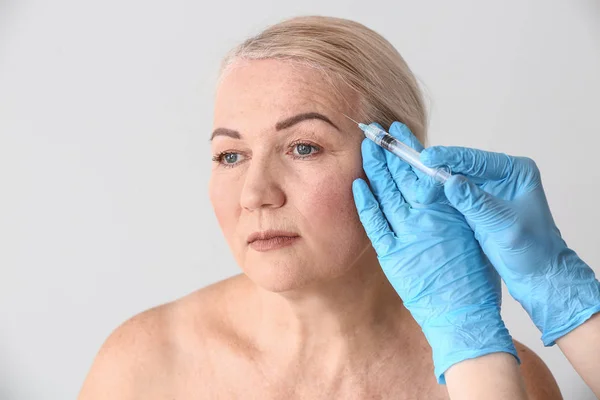 Rijpe vrouw ontvangen injectie in gezicht op lichte achtergrond — Stockfoto