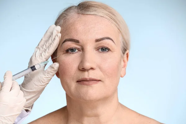 Rijpe vrouw ontvangen injectie in gezicht op kleur achtergrond — Stockfoto
