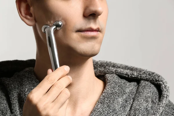 Man with facial massage tool on light background, closeup — Stock Photo, Image