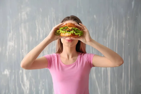 Schöne, glückliche junge Frau mit leckerem Burger auf grauem Hintergrund — Stockfoto