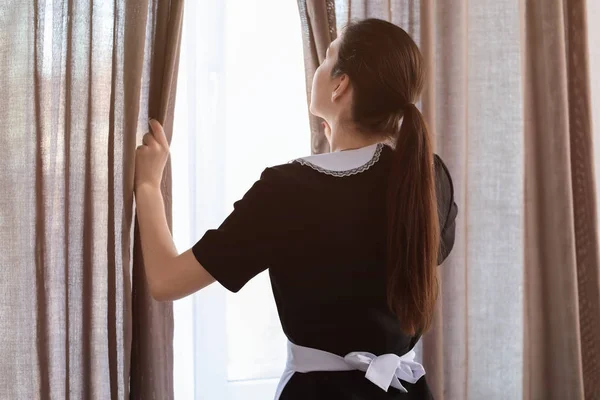 Vrouwelijke huishoudster gordijnen op venster openen in kamer — Stockfoto