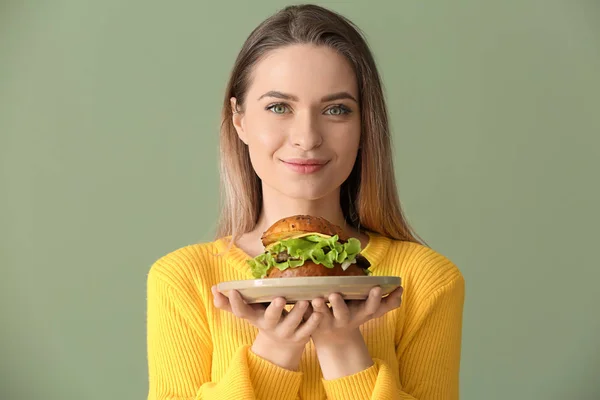 Beautiful young woman with tasty burger on color background — Stock Photo, Image