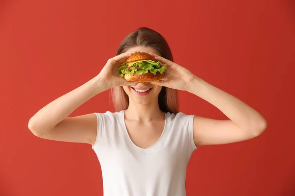 Beautiful happy young woman with tasty burger on color background — Stock Photo, Image