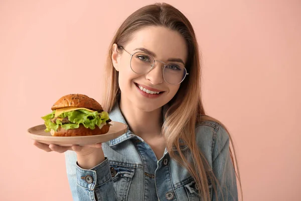 Beautiful young woman with tasty burger on color background — Stock Photo, Image