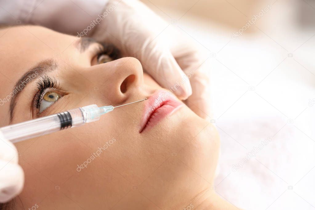 Young woman receiving filler injection in beauty salon