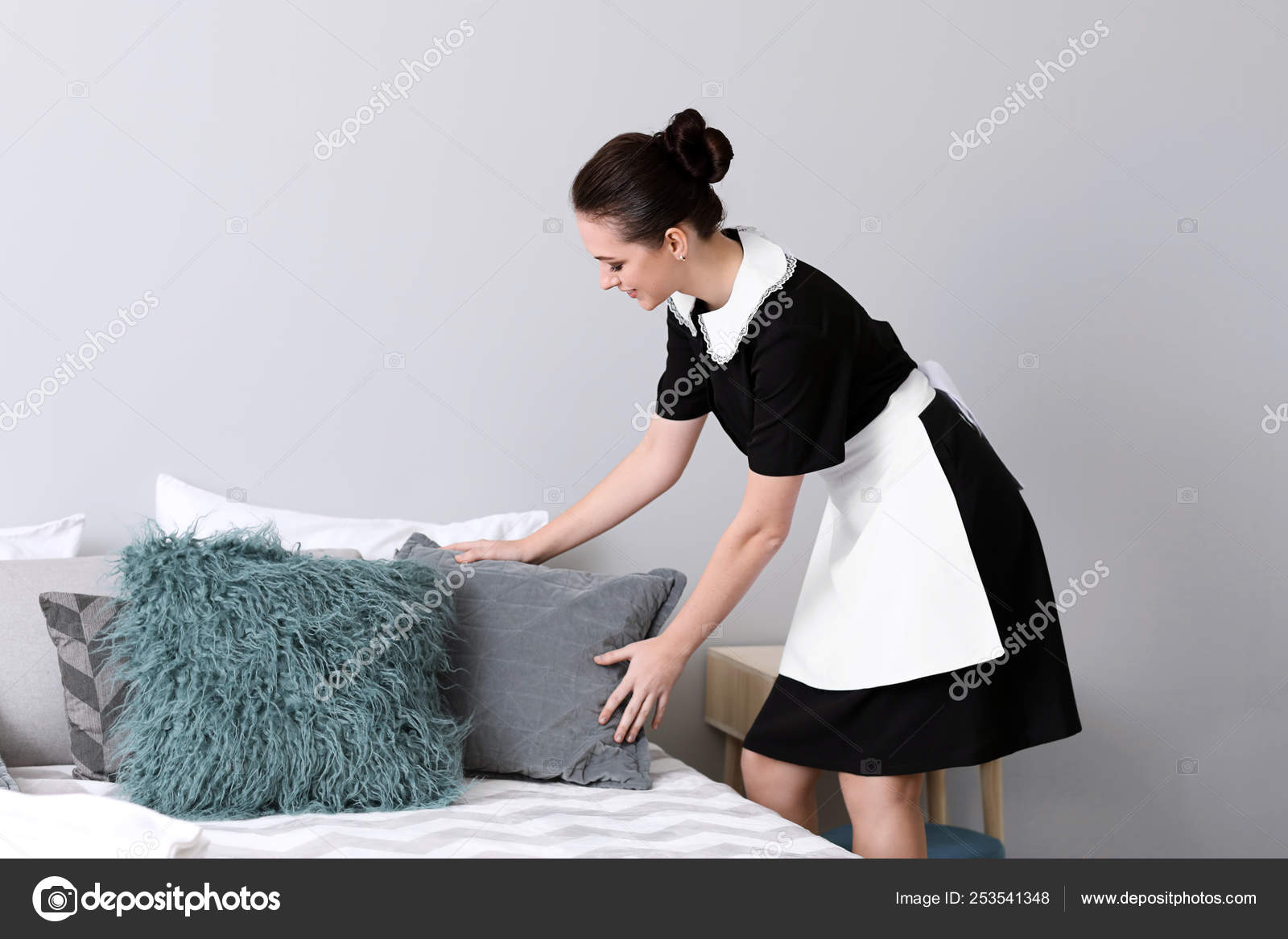 Beautiful female housekeeper making bed in room Stock Photo by