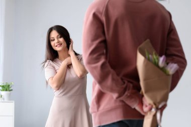 Genç adam karısı için buket çiçek saklanıyor. 8 Mart kutlama