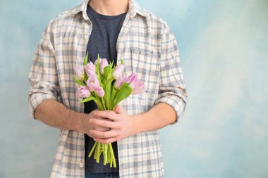 Buket çiçek ışık arka plan üzerinde olan genç adam. 8 Mart kutlama