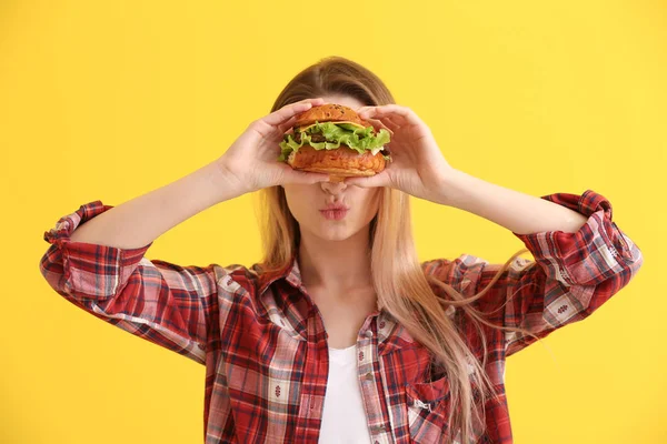 Beautiful happy young woman with tasty burger on color background — Stock Photo, Image