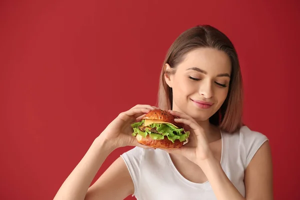 Schöne junge Frau mit leckerem Burger auf farbigem Hintergrund — Stockfoto
