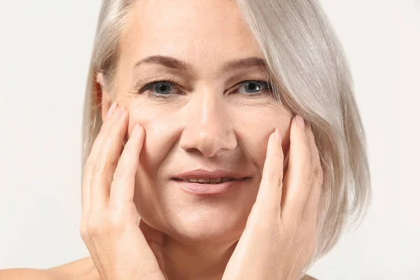 Mature woman giving herself face massage on light background — Stock Photo, Image