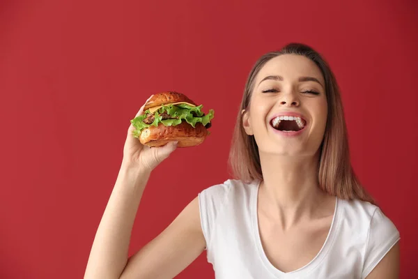 Schöne glückliche junge Frau mit leckerem Burger auf farbigem Hintergrund — Stockfoto